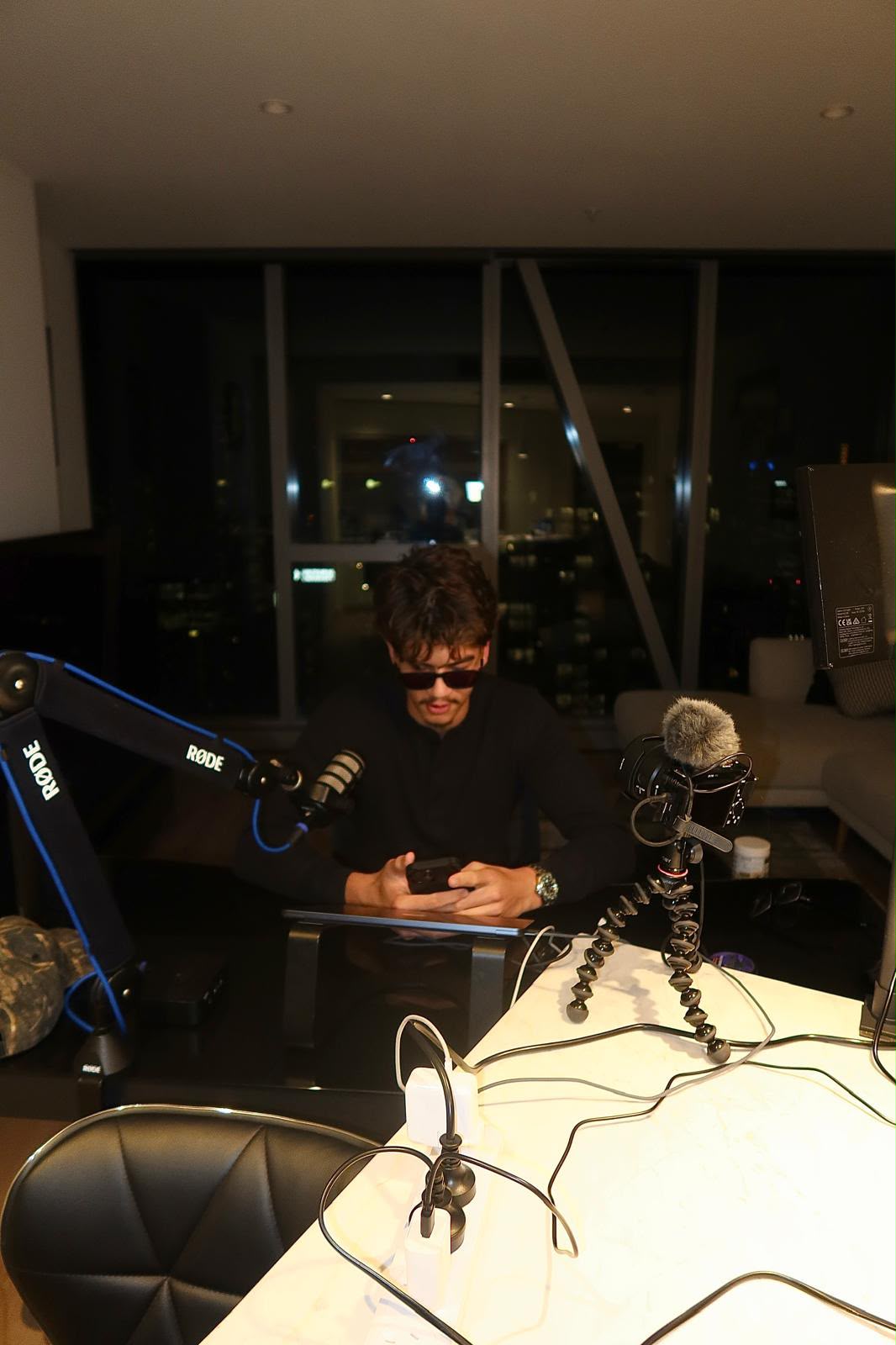 Huddy at his desk late at night, phone in both hands, microphone and camera set up beside him.