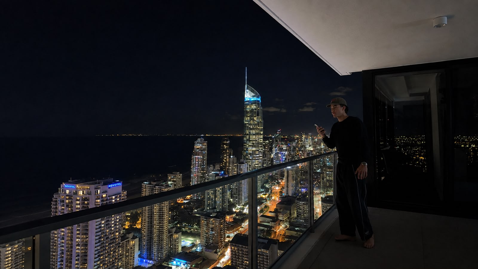 Huddy on a high-rise balcony at night, the Gold Coast skyline lit up behind him.